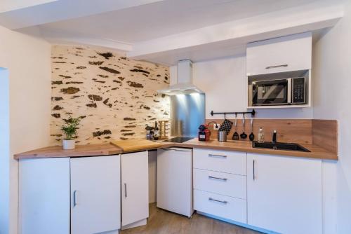 uma cozinha com armários brancos e uma parede de pedra em Logement Duplex au cœur de Tréguier em Tréguier