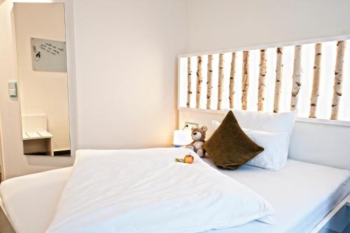 a white bed with a teddy bear sitting on it at Hotel Jungstil in Darmstadt