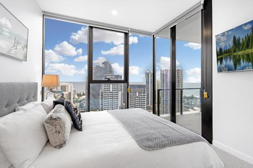 a bedroom with a white bed and large windows at Lamour Ocean View Apartment II in Casino Broadbeach - free parking-195cm in Gold Coast