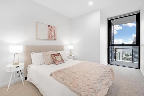 a white bedroom with a large bed and a window at Lamour Ocean View Apartment I in Casino Broadbeach - free parking in Gold Coast