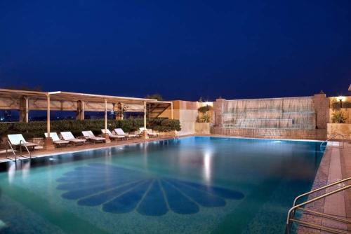 una gran piscina por la noche con tumbonas en The Bristol, en Gurgaon