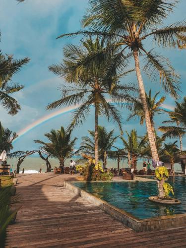 a rainbow over a beach with palm trees and a pool at Pousada Vila do Mar in Caraíva