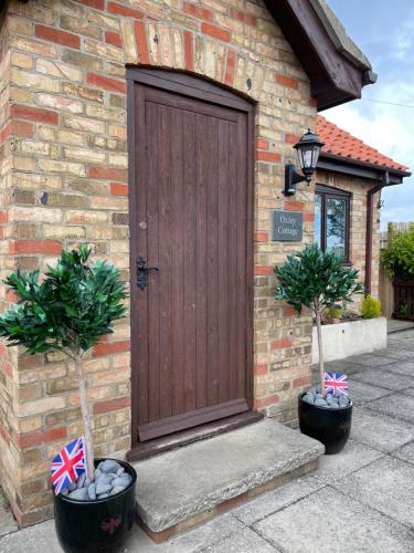 uma porta de madeira num edifício de tijolos com duas plantas em Oxley Cottage em Alford