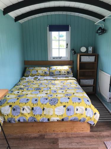 a bedroom with a bed with a yellow comforter with fishes at Shepherds Hut (Benny's) in Cullompton