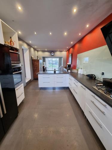 une grande cuisine avec des placards blancs et un mur orange. dans l'établissement Villa de la gare, à Montbazin