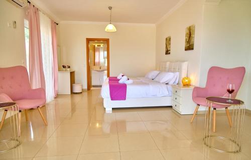 a bedroom with a bed and two pink chairs at Villa Spiros Imerolia Kassiopi in Kassiopi