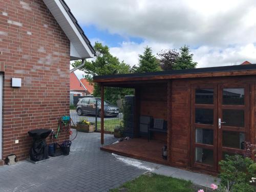 a wooden shed with a wooden deck next to a house at Feriendomizil Dornum Haus Margarete mit Wallbox in Dornum