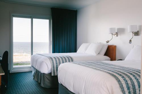 two beds in a hotel room with a view of the ocean at Pavillon sur Mer par Riôtel in Matane