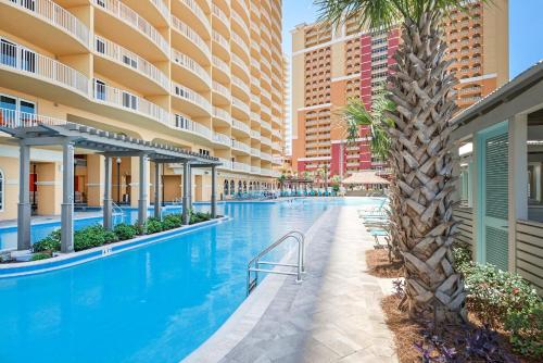 an infinity pool with a palm tree and buildings at Calypso 3-406 - Paradise by the Pier in Panama City Beach