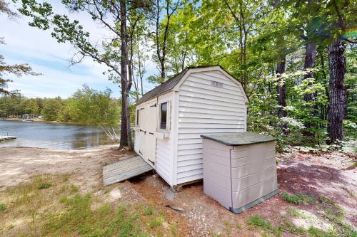 a small white outhouse with a trashcan next to a river at Lake House Retreat in Ossipee