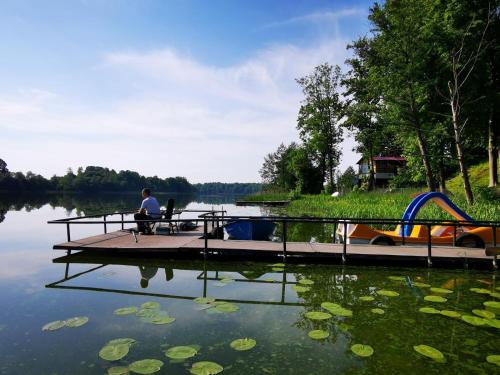 a person sitting at a picnic table on a dock on a lake at Urocza Przystan in Kiemiany