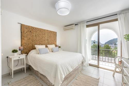 a white bedroom with a bed and a large window at Casita en Cala Llonga in Cala Llonga