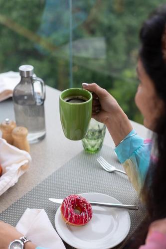 a woman holding a cup of coffee and a donut on a table at The Oasis Mussoorie - A Member of Radisson Individuals in Mussoorie