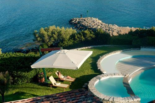 eine Frau auf einem Stuhl unter einem Regenschirm neben einem Pool in der Unterkunft Hotel Palumbalza Porto Rotondo in Porto Rotondo