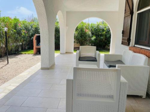 an outdoor patio with white chairs and an archway at Villino Oleandro a pochi passi dalla spiaggia di Simius in Simius
