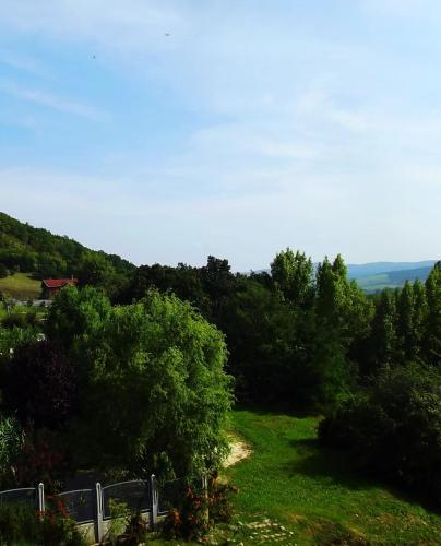 a grassy hill with trees and a house in the distance at Tündérszikla Panzió in Pilisjászfalu