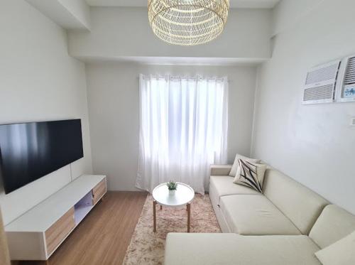 sala de estar blanca con sofá y TV en Lovely 2- BR Condo (Fully Air-conditioned w/ Wifi), en Cagayan de Oro