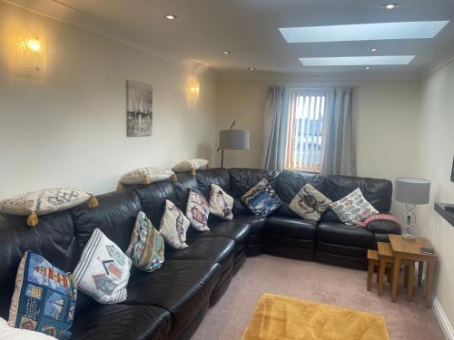 a living room with a black leather couch with pillows at THE CARRIAGE HOUSE in Woodhorn