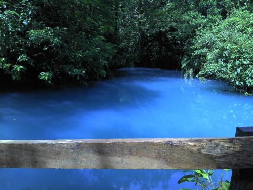 a blue river with a wooden fence in front of it at Hospedaje Rio Celeste Katira, Habitación privada in San Rafael