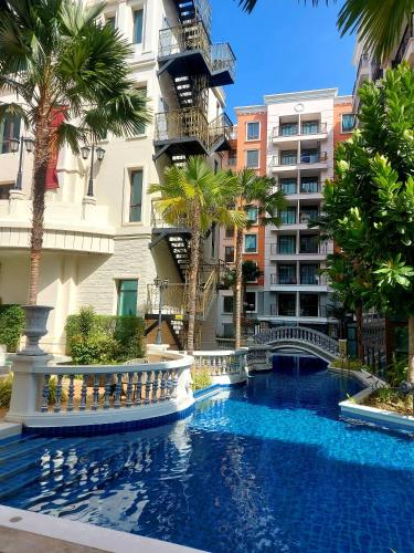 a swimming pool in front of a building with palm trees at Espana Resort Pattaya Jomtien in Jomtien Beach