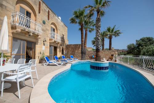 una piscina con sillas, una mesa y palmeras en Blossom Farmhouses, en Għasri