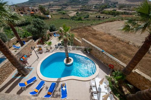 a pool at a resort with chairs and a palm tree at Blossom Farmhouses in Għasri