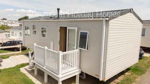 a small white tiny house with a porch at 2021 2 Bedroom Deluxe Caravan Sleeps 6 with WI-FI in Wyke Regis