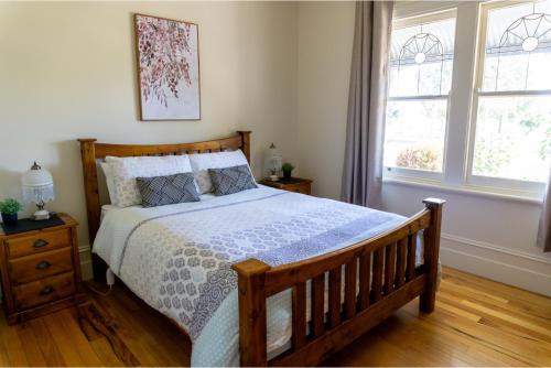 a bedroom with a bed with a wooden bed frame and two windows at Pound Hill Cottage in Miners Rest