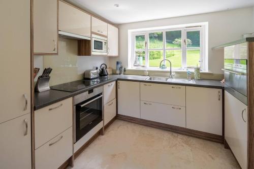 a kitchen with white cabinets and a sink and a window at Osbornes Holiday House near Exeter with swimming pool in Exeter