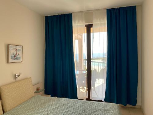 a bedroom with a bed and a window with blue curtains at Kaliakria Infinity Pool Apartment in Topola