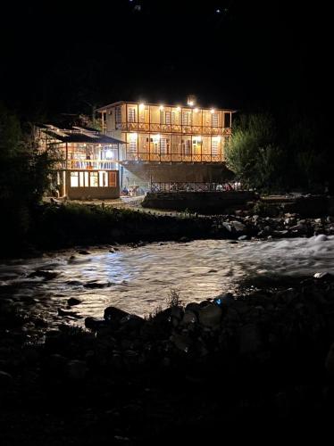 a building lit up at night next to a river at Living Good - A Himalayan Boutique Stay in Gushaini