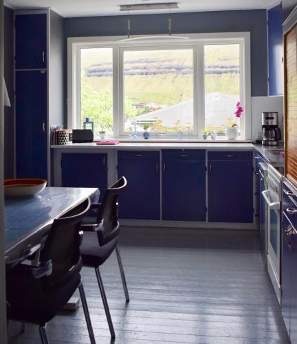 a kitchen with blue cabinets and a large window at Brekkustova - Modern, cosy and spacious apartment in Klaksvík