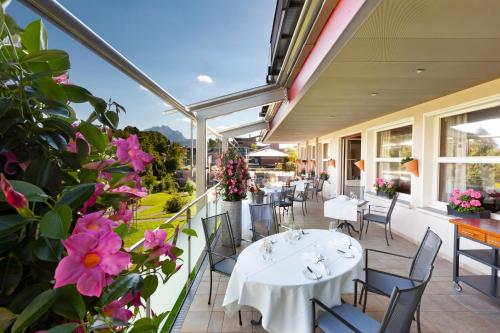 eine Terrasse mit weißen Tischen und Stühlen sowie rosafarbenen Blumen in der Unterkunft Hotel Balm in Luzern