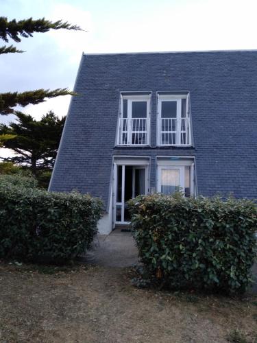 una casa de techo azul con ventanas blancas y arbustos en Charmant logement vue mer avec chambre et terrasse en Guidel