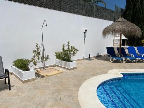 a swimming pool with blue chairs next to a white wall at Villa Maravilla in Murcia