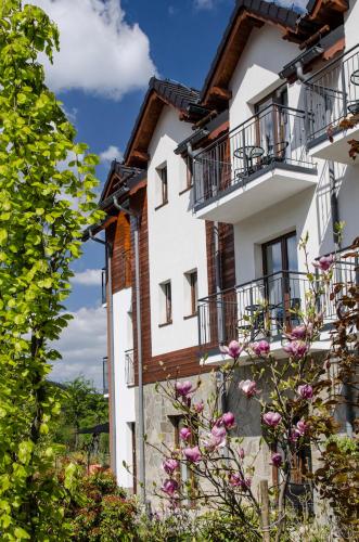 a white building with balconies and flowers at Karkonoskie Widoki - Jacuzzi z widokiem na Śnieżkę - pyszne śniadania i parking w cenie - pokoje z balkonami in Karpacz