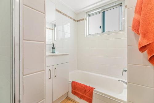 La salle de bains blanche est pourvue d'une baignoire et d'une fenêtre. dans l'établissement Rainbow Pacific Unit 8, à Gold Coast