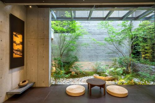 a room with two tables and two stools in front of a garden at Genji Kyoto, a Member of Design Hotels in Kyoto