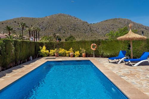 a swimming pool with two blue chairs and an umbrella at Villa Iris - Alcúdia in Alcudia