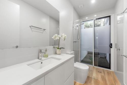 a white bathroom with a toilet and a sink at Waves Beach House in Marcoola