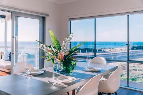 Una mesa con sillas y un jarrón de flores encima. en ōSHEN - Sleeps12 Gym Kayak MountnBike BeachFrnt, en Aldinga Beach