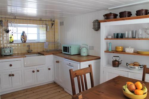 a kitchen with white cabinets and a table with a bowl of fruit at Teana Cottage in Polperro