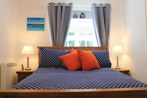 a bed with blue and orange pillows in front of a window at Teana Cottage in Polperro