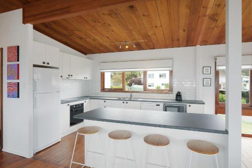 a kitchen with white cabinets and a counter with stools at 17 Dulling Street Beach House in Dalmeny