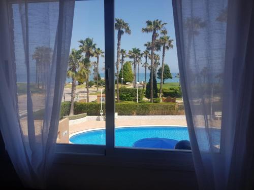 a window with a view of a pool and palm trees at Magic World Frontal 1ª línea in Oropesa del Mar