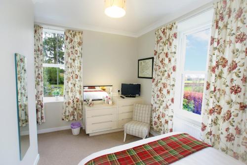 a bedroom with a bed and a tv and two windows at Craignair Cottage in Dalbeattie