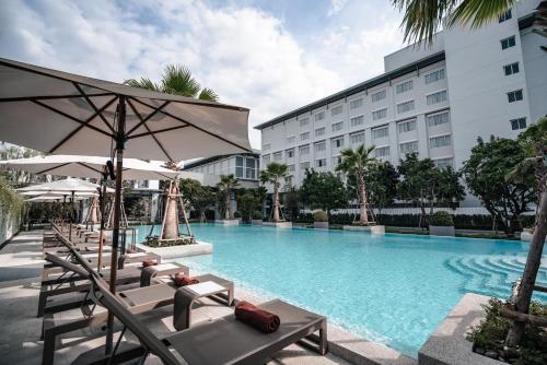 a swimming pool with chairs and umbrellas in front of a building at Health Land Resort & Spa in Pattaya South