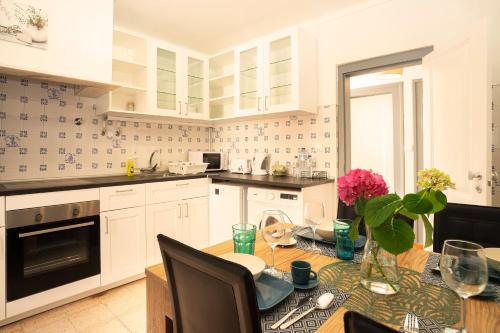 a kitchen with white cabinets and a table with pink flowers at Happy Holiday Cascais - Garden in Cascais