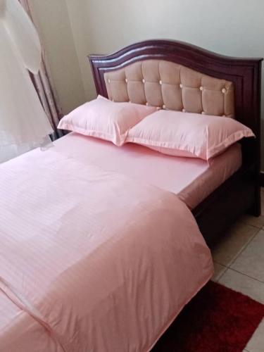 a large bed with pink sheets and pillows on it at Candle Wood Homes in Lira