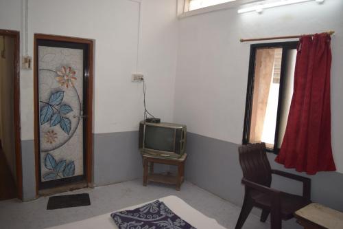a room with a tv and a chair and a window at Hotel Gokarn Lodging in Satara
